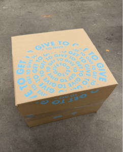 A Give to Get Purpose Pack, a cardboard box with concentric circles of light blue text that read Give To Get